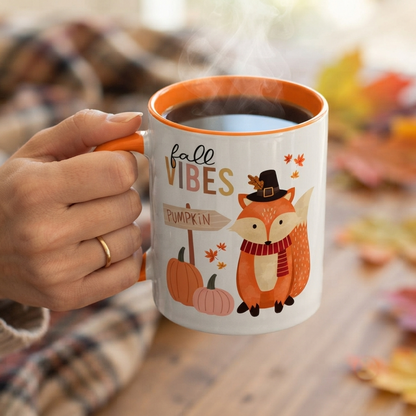 Fall Vibes Fox Mug featuring a cute fox wearing a pilgrim-style hat and scarf beside pumpkins and a pumpkin sign, printed on a white ceramic mug with an orange handle and orange interior. Perfect for fall coffee, tea, Thanksgiving, and autumn home décor.