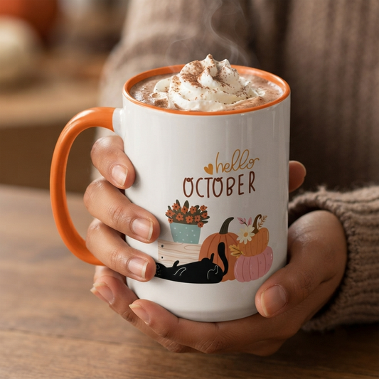 Hello October ceramic accent mug featuring a black cat relaxing beside pumpkins and autumn flowers, available in pink and orange accent colors in 11oz and 15oz sizes.